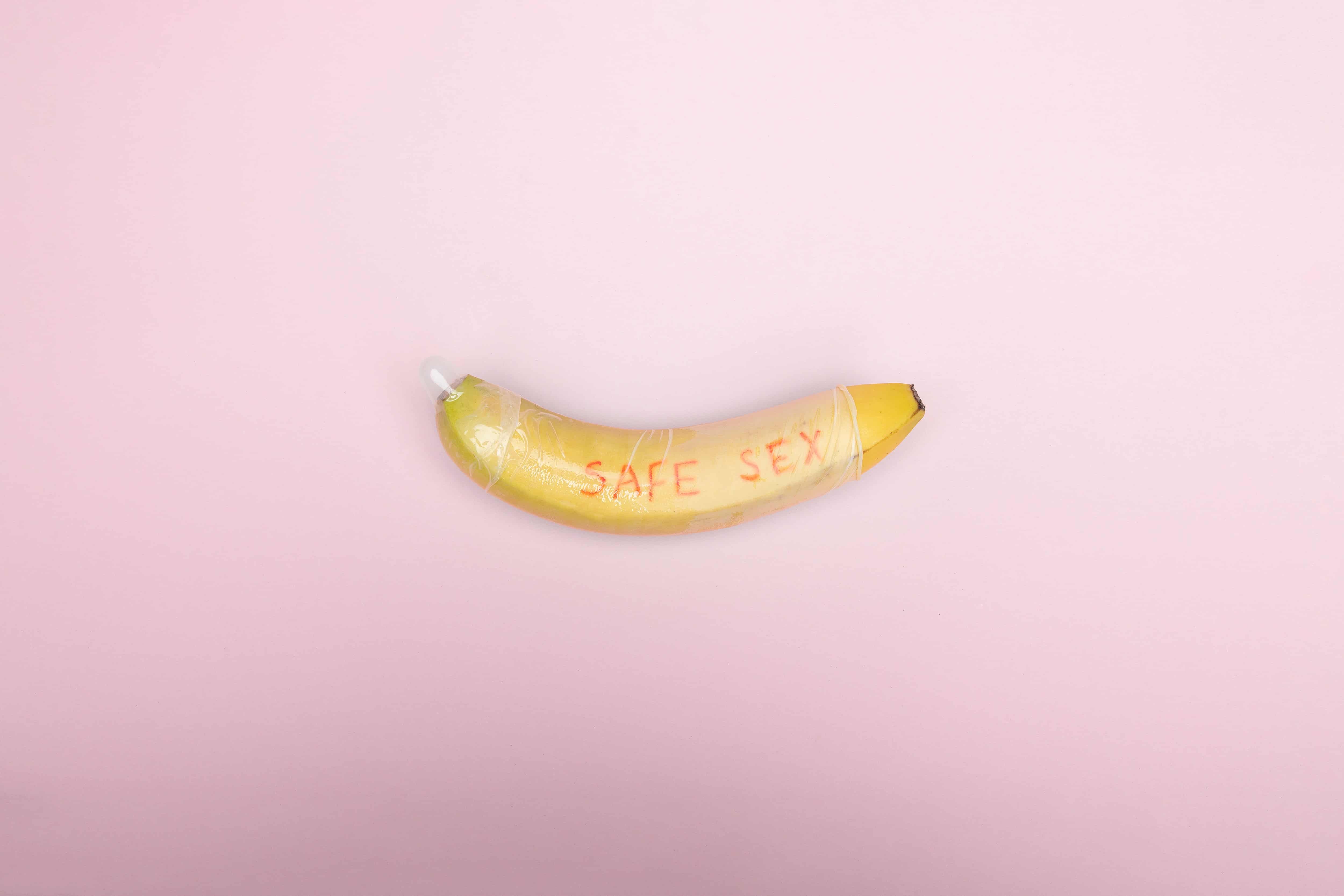 Picture of a banana in a condom on a pink background